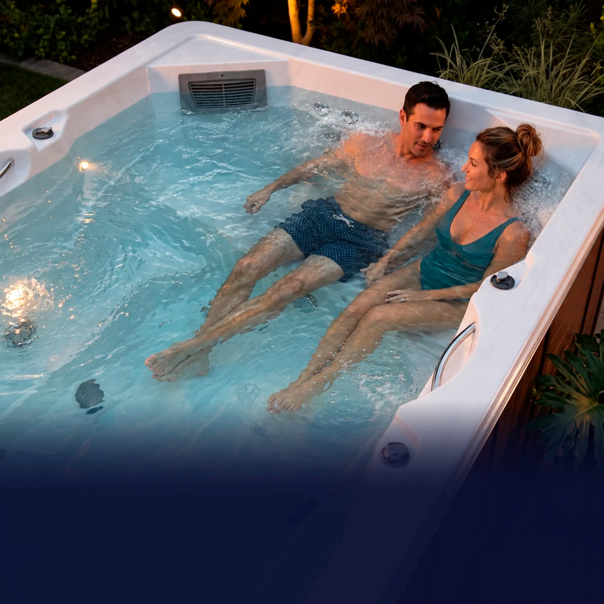 Pareja disfrutando del hidromasaje en un swim spa exterior con jets activos
